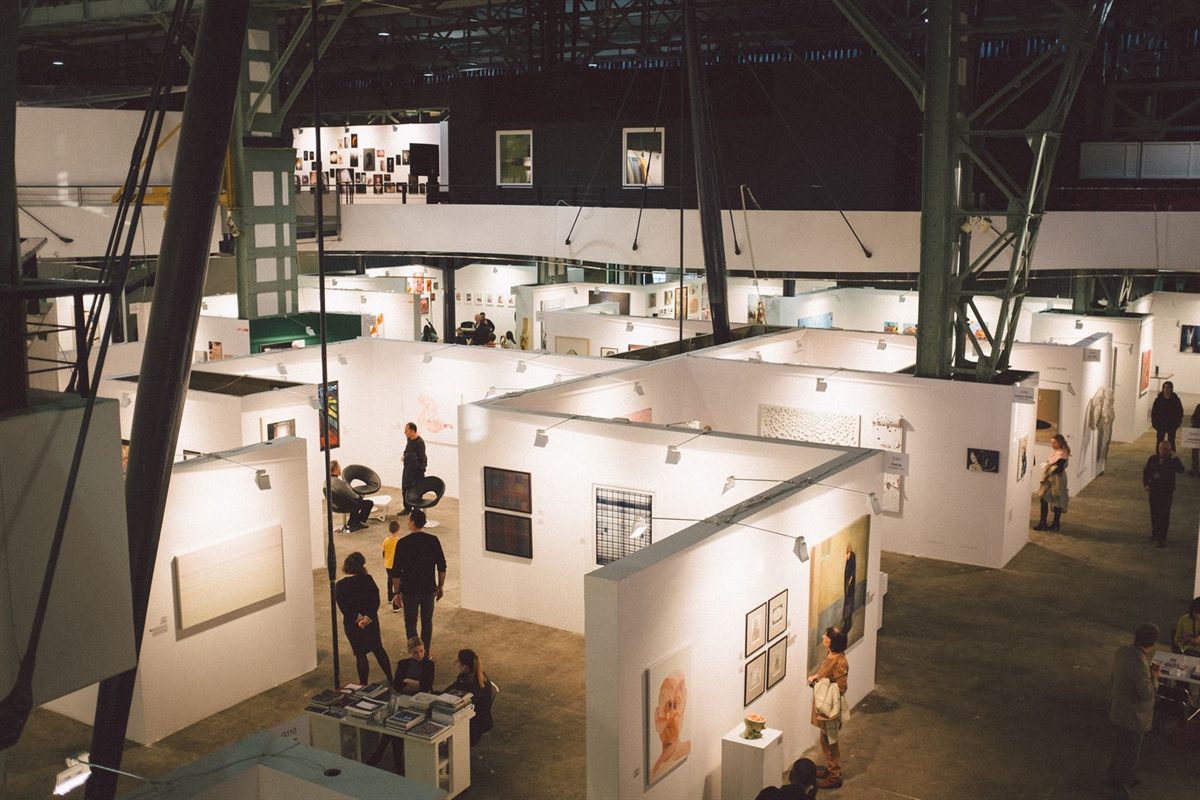 Looking down on rows of white exhibition stands and visitors in a large hall
