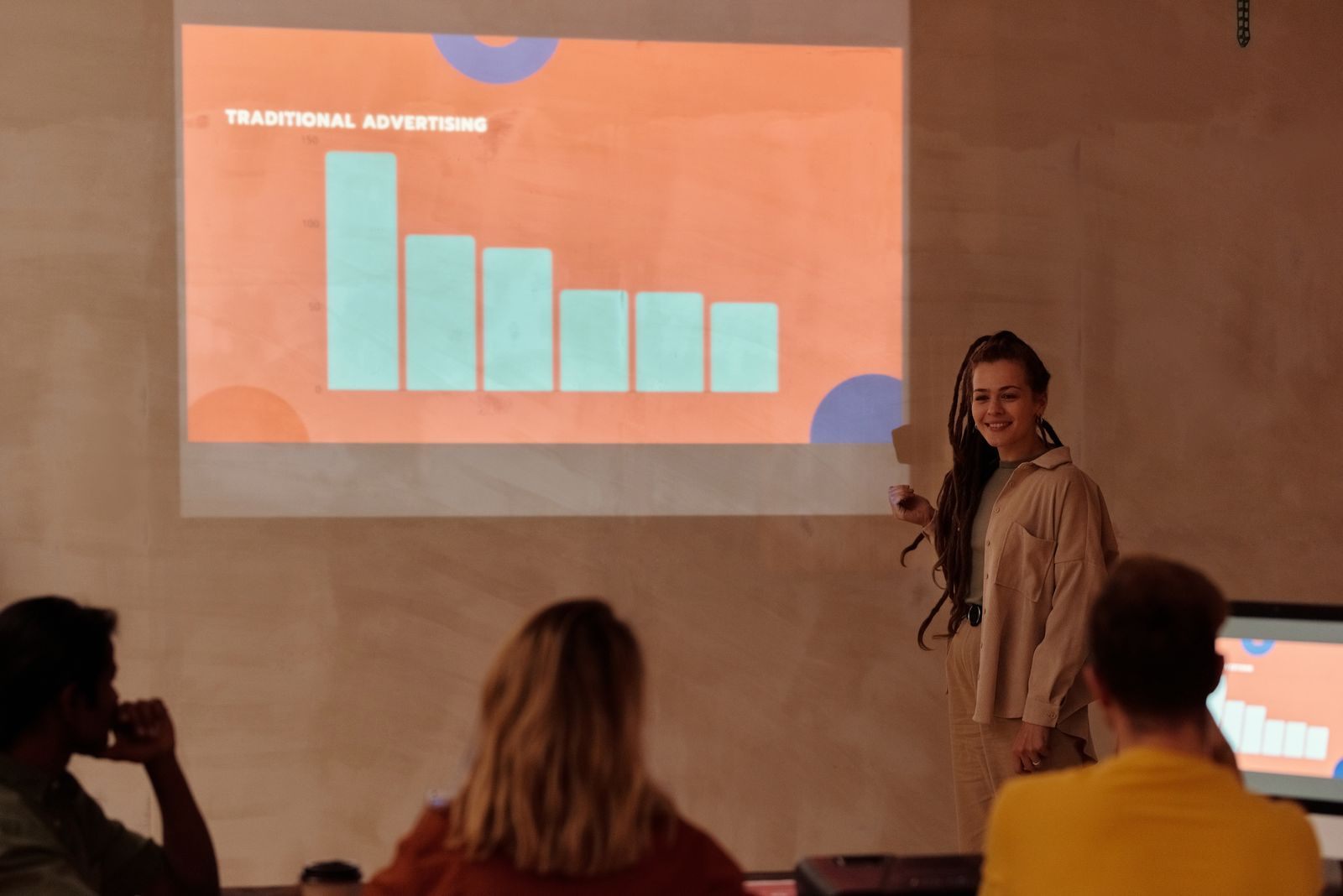 A presenter stands beside a projected chart while a small audience listens, like a supplier session at travel agent events