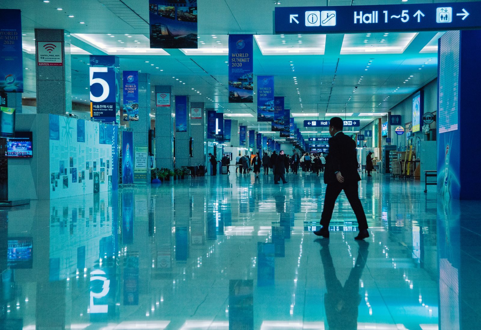 A long, bright exhibition centre concourse with hall signs, the kind of venue that hosts travel trade shows